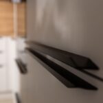 Čierne kovové profilové úchytky na bielych matných dvierkach vysokej kuchynskej skrine.
