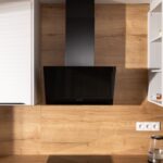 Čierny moderný digestor nad indukčnou varnou doskou s dreveným stenovým panelom v pozadí.