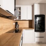 Biela kuchynská linka s dubovou pracovnou doskou, indukčnou varnou doskou a čiernou dizajnovou digestorovou plochou.