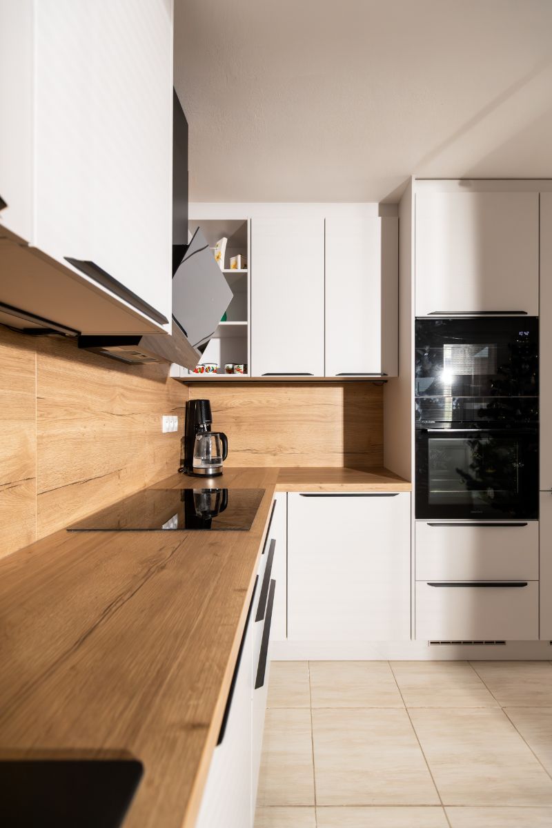 Biela kuchynská linka s dubovou pracovnou doskou, indukčnou varnou doskou a čiernou dizajnovou digestorovou plochou.
