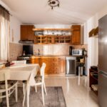 Kuchyňa s tradičným dreveným nábytkom, bielym jedálenským stolom a béžovou dlažbou v rustikálnom štýle.