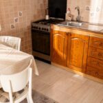 Interiér staršej kuchyne s plynovým sporákom, dreveným nábytkom a svetlou keramickou dlažbou.