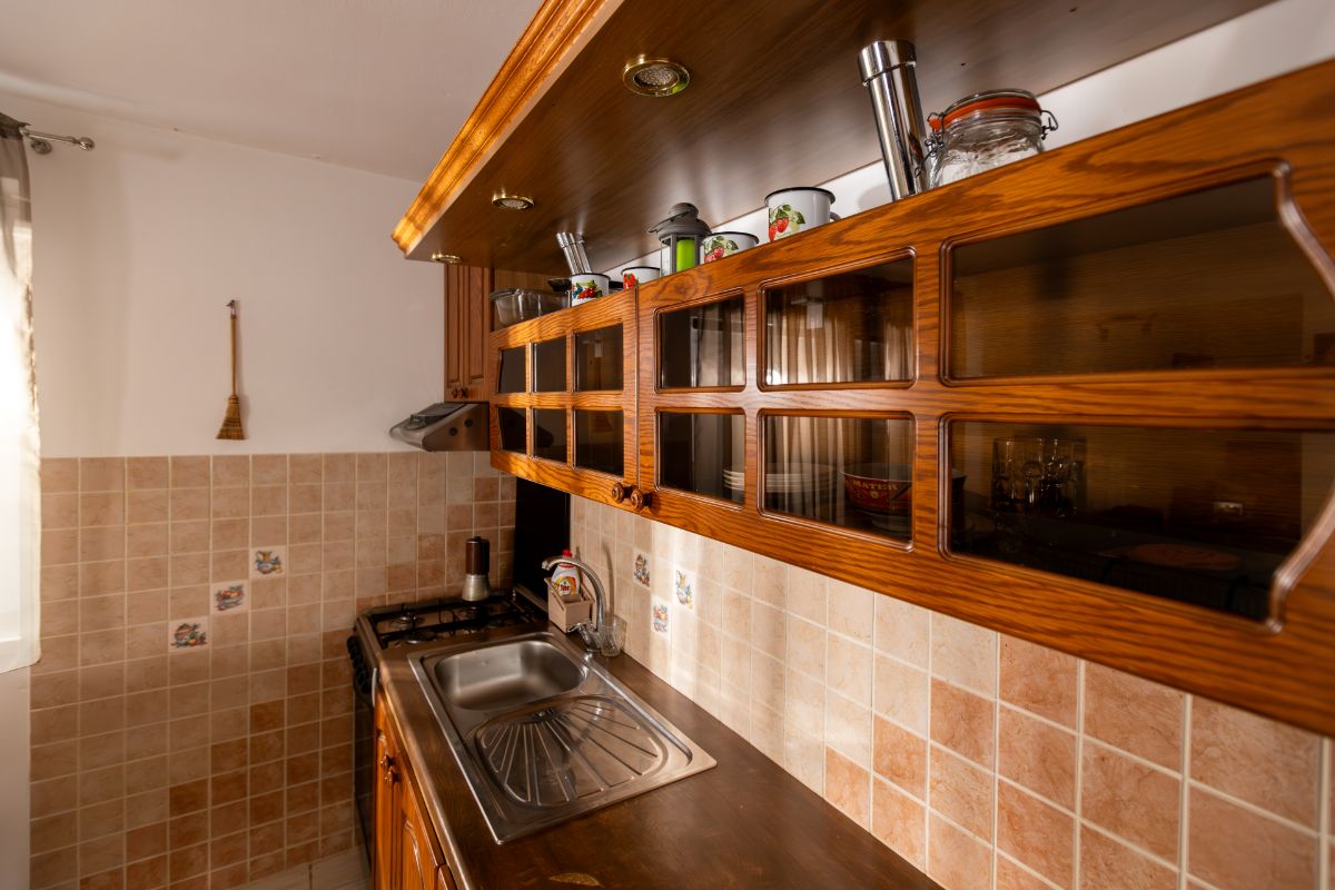 Horné skrinky kuchynskej linky s presklenými dvierkami a zabudovanými bodovými svetlami v drevenej rampe.