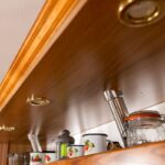 Drevená svetelná rampa s mosadznými bodovými svietidlami nad hornými policami kuchynskej linky.