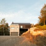 Moderná chata s kontrastným tmavým a svetlým dreveným obkladom a garážou v prírodnom prostredí.