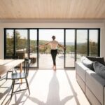 Presvetlená obývačka s posuvnou sklenenou stenou, drevenou podlahou a výhľadom na terasu a prírodu.