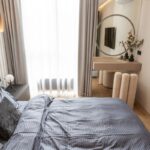 Moderná spálňa so sivou posteľnou bielizňou a minimalistickým toaletným stolíkom pri bielom lamelovom obklade steny.