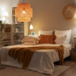 Útulná spálňa s pletenou horčicovou dekou a vrstveným ratanovým svietidlom v blízkosti bielych knižníc.