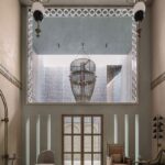 Presvetlená hala s vysokým stropom, korálikovým lustrom a mramorovou dlažbou.