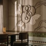 Nástenná dekorácia s motívom motýľov nad dreveným stolom a zeleným keramickým obkladom.