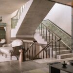 Elegantné schodisko s mosadzným zábradlím, zeleným obkladom a štýlovým krémovým kreslom.