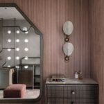 Tmavá drevená komoda s mramorovou doskou pod zrkadlom na rastrovej ružovej stene.