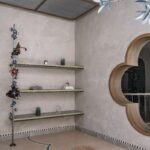 Minimalistický kút s betónovými policami, oblúkovým oknom a jemnou mozaikovou bordúrou.