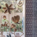 Umelecké prútené svietidlá v tvare kvetov pred veľkoformátovým oknom s výhľadom do exotickej záhrady.