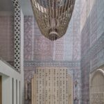 Mohutný drevený korálikový luster v interiéri s dekoratívnou tapetou a dizajnovou skriňou.