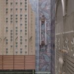 Svetlá drevená skriňa s modrým šnurovaním a mosadzné nástenné svietniky na vzorovanej tapete.