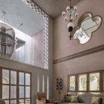 Vysoká obývacia izba s ružovkastou stierkou, zelenou pohovkou a visiacimi mosadznými lustrami.