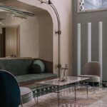 Oblúkový priechod s textúrou, zelená čalúnená lavica a mramorový stolík na geometrickom koberci.