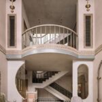 Interiér s galériou, oblúkovým balkónom, bielym schodiskom a dizajnovým nábytkom v zemitých tónoch.