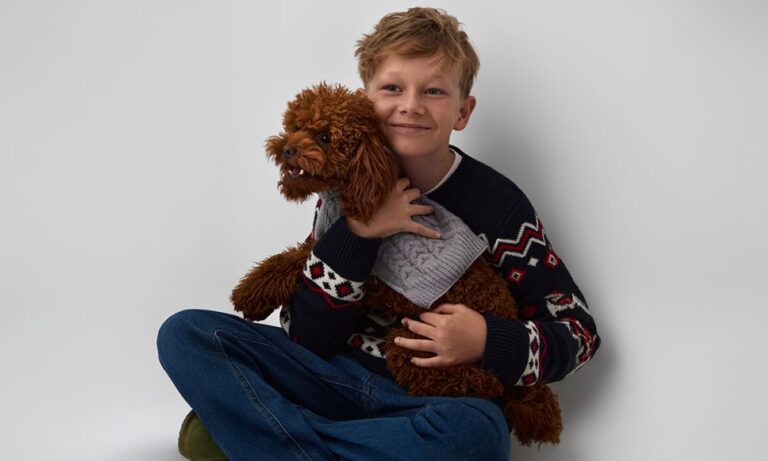 Malý chlapec držiaci psa s pleteným svetrom.