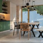 Jedálenský kút s masívnym dreveným stolom, čiernymi stoličkami, zelenou kuchynskou linkou a veľkoformátovou sivou dlažbou.