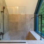 Sprchový kút so sivým kamenným obkladom, matnými čiernymi batériami a presklenou stenou.