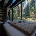 Minimalistická spálňa s panoramatickým oknom v čiernom ráme a exteriérovou lesnou kulisou.