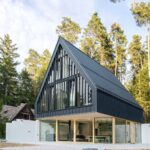 Moderný dom s čiernym plechovým obkladom, veľkoformátovými sklenenými stenami a svetlým dreveným podhľadom.