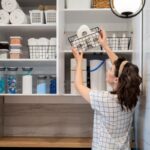 Žena ukladá do skrinky v kúpeľni košík s toaletným papierom.