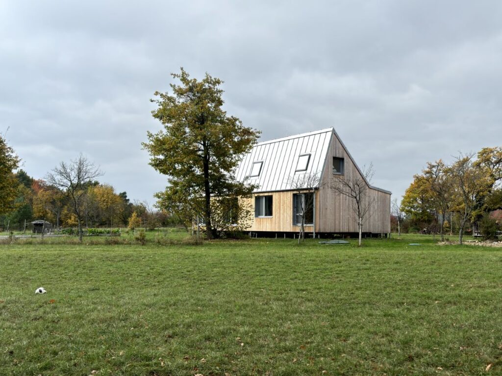 Moderný drevený dom so svetlou šikmou plechovou strechou a strešnými oknami.
