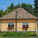 Starý vidiecky dom na dedine so šikmou strechou a muškátmi v oknách.