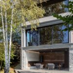 Dvojposchodový dom s veľkými čiernymi oknami a kamennou fasádou pri breze.