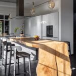 Moderná biela kuchyňa s masívnym dreveným ostrovčekom a tmavou drevenou parketovou podlahou.