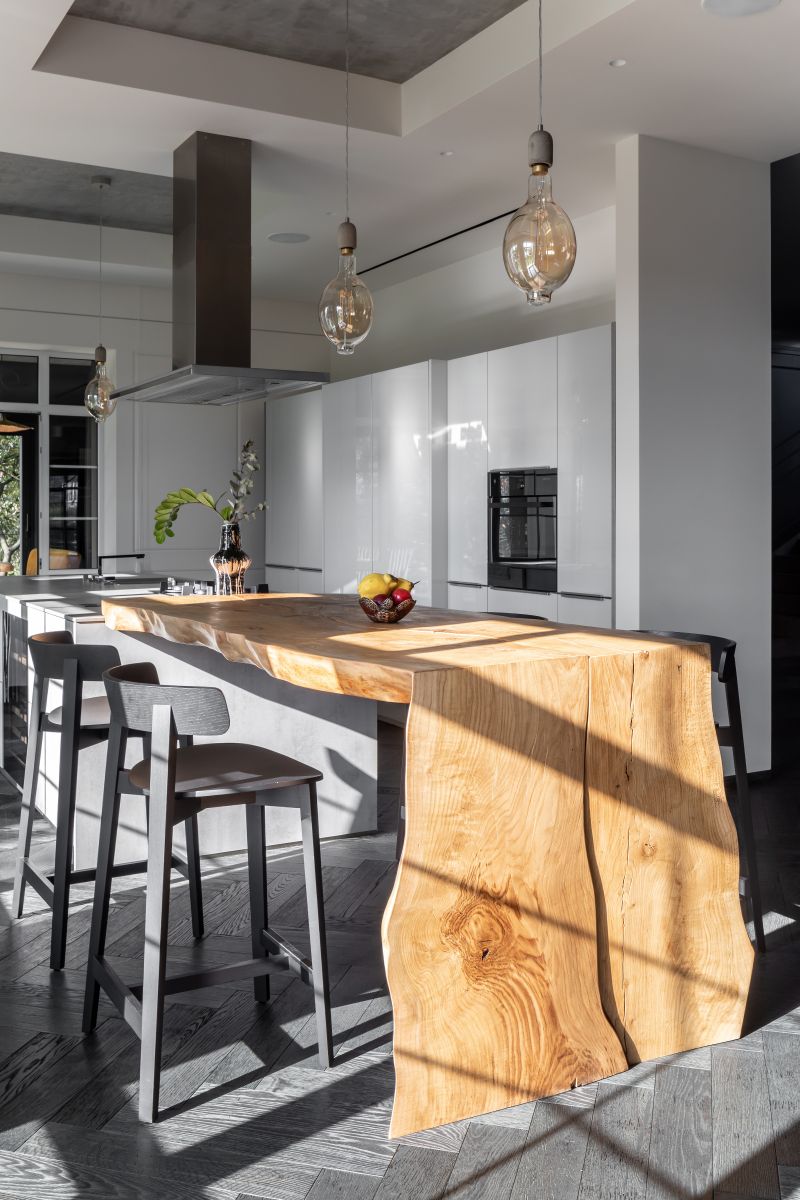 Moderná biela kuchyňa s masívnym dreveným ostrovčekom a tmavou drevenou parketovou podlahou.