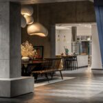 Tmavý industriálny interiér s vysokými betónovými stĺpmi, drevenou podlahou so vzorom a moderným závesným svietidlom.