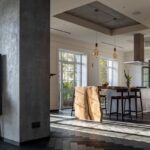 Moderný interiér s betónovými stenami, dreveným ostrovčekom a sklenenými posuvnými dverami do záhrady.