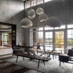 Vysoká jedáleň s betónovými stenami, veľkými oknami a bielymi dizajnovými lampami nad stolom.