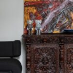 Vyrezávaná tmavohnedá komoda so soškami KAWS pred abstraktným farebným obrazom.