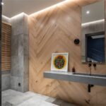 Toaleta s dreveným obkladom s motívom rybej kosti a stenami z kameňa s liatym sivým umývadlom.