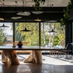 Jedáleň s betónovou podlahou, hrubým dreveným stolom na masívnych pňoch a modernými čiernymi závesnými lampam