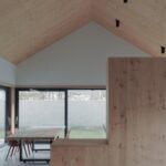 Interiér s drevom obloženým šikmým stropom, dreveným stolom a červenými stoličkami pri okne.