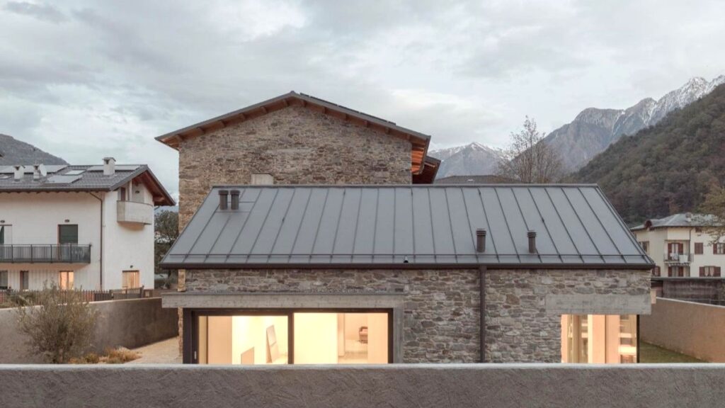 Vonkajší pohľad na kamenný dom s plechovou strechou a veľkými oknami s výhľadom na hory.