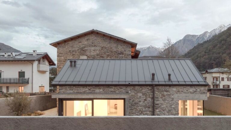 Vonkajší pohľad na kamenný dom s plechovou strechou a veľkými oknami s výhľadom na hory.