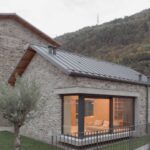 Dom so sedlovou strechou, kamennou fasádou a rohovým presklením s dverami na malú terasu.