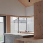 Interiér s dreveným šikmým stropom a betónovou kuchynskou linkou s drevenými skrinkami pri veľkom okne.