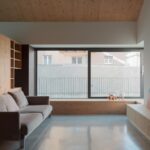 Obývačka s dreveným obkladom, šedou lesklou podlahou a béžovou pohovkou pri okne.