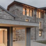 Kamenný dom s tmavou strechou a modernou betónovou terasou podopretou betónovým stĺpom.