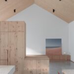 Interiér s vysokým šikmým dreveným stropom, vstavanými drevenými skrinkami a sivou podlahou.