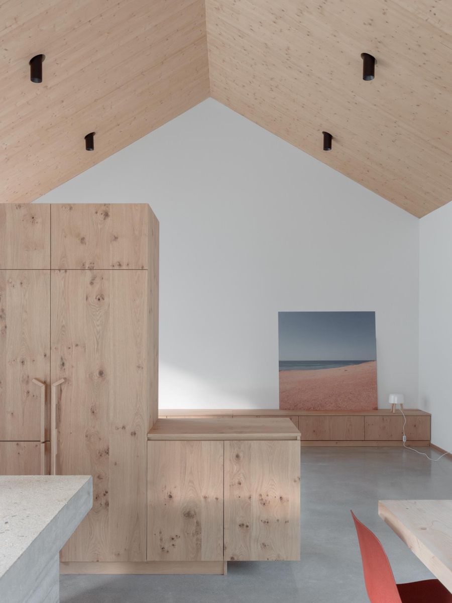 Interiér s vysokým šikmým dreveným stropom, vstavanými drevenými skrinkami a sivou podlahou.