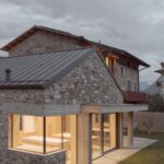 Exteriér kamenného domu s plechovou strechou a presvetlenou prístavbou s veľkými oknami.